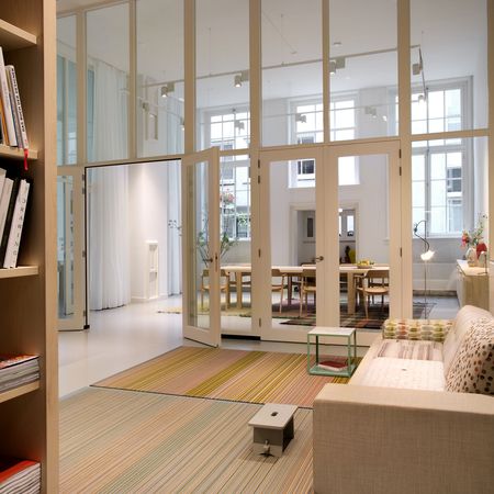 Ein modernes, minimalistisches Wohnzimmer mit bunt gestreiften Teppichen, einem beigen Sofa, einem kleinen Couchtisch