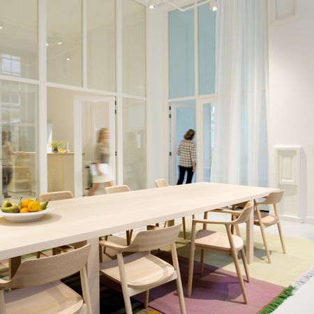 Ein hölzerner Esstisch mit hellen Stühlen, umgeben von bunt gemusterten Teppichen in Rosa-, Grün- und Karo-Tönen