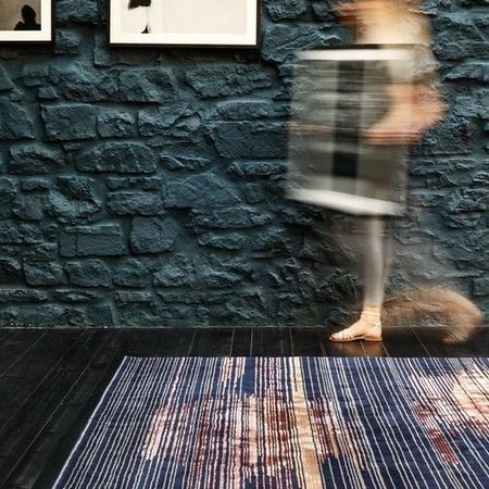 Eine verschwommene Gestalt geht über einen bunten Teppich auf einem dunklen Holzboden