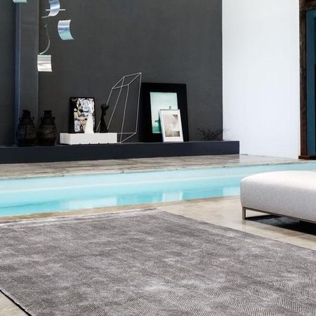 Moderner Wohnraum mit einer grauen Wand, minimalistischem Dekor, einem hellblauen Pool und einem strukturierten Teppich