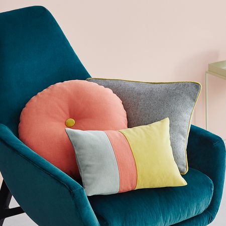 Ein blaugrüner Sessel mit bunten Kissen vor einem pastellfarbenen Hintergrund