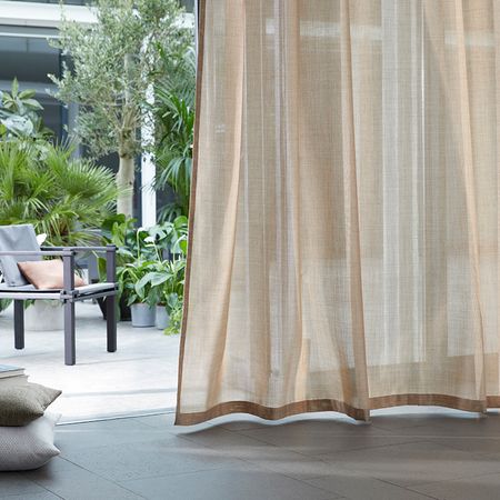 Helle, luftige Vorhänge umrahmen eine ruhige Terrasse mit üppigen Pflanzen und einem gemütlichen Stuhl