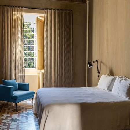 Helles Schlafzimmer mit weißer Tagesdecke, blauem Sessel und gemustertem Bodenbelag