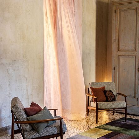 Gemütliches Interieur mit zwei gemusterten Sesseln, einem farbenfrohen Teppich und weichen Vorhängen