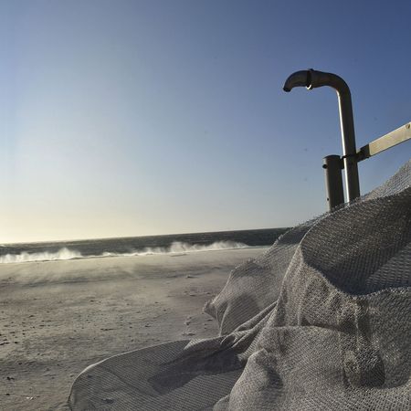 Ein strukturiertes Fischernetz hängt über dem vom Sonnenlicht beleuchteten Sandstrand