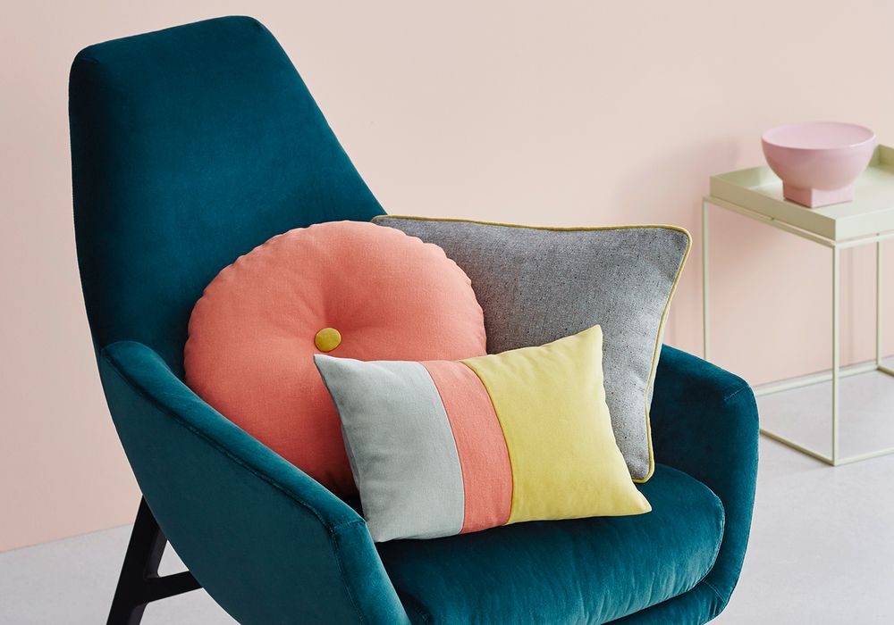 Ein tealfarbener Sessel mit gemütlichen Kissen in Rosa, Grau und einem bunten Streifenmuster