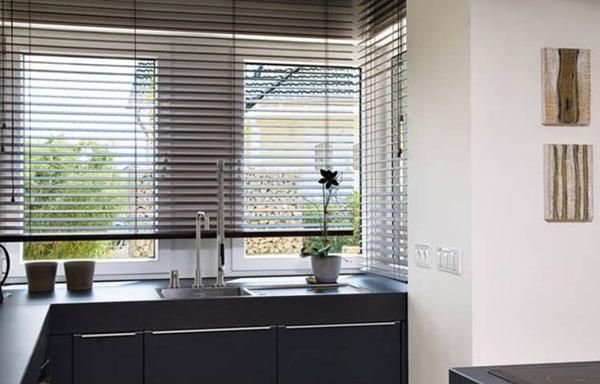 Moderne Küche mit schlichten schwarzen Schränken, einem Fenster mit horizontalen Jalousien und einer Topfpflanze neben dem Waschbecken