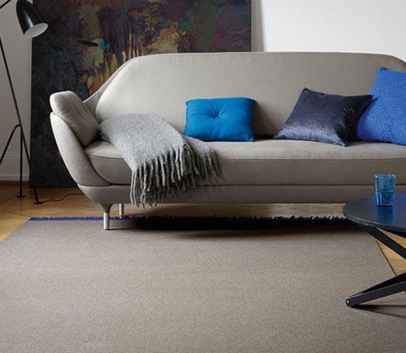 Ein modernes graues Sofa mit bunten Kissen und einer Decke, mit einem schlichten schwarzen Beistelltisch auf einem beigen Teppich