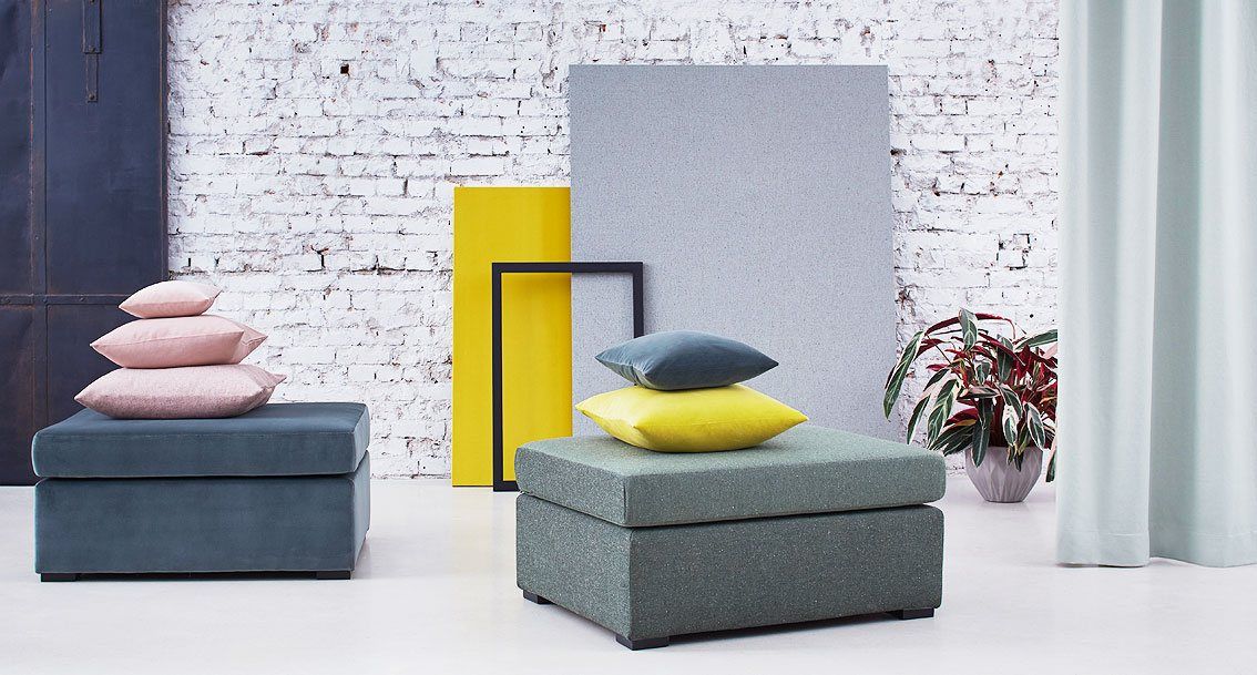 Zwei moderne Ottomane in Grün und Blau mit gestapelten rosa Kissen